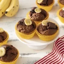 Foto da receita de Muffin de Banana com Chocolate Caribe. Observa-se 8 muffins em forminhas amarelas com uma rodela de banana e metade de um bombom no topo.