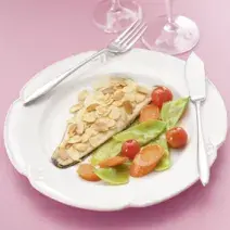 Fotografia em tons de rosa em uma mesa de madeira rosa com um prato branco raso e um filé de truta com amêndoas laminadas e salada dentro dele.