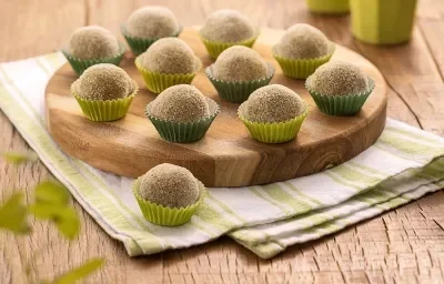 Foto da receita de Brigadeiro de Batata Doce. Na foto, observa-se brigadeiros em forminas nos tons de verde, sobre uma tábua redonda de madeira e um guardanapo listrado. Foto da receita de Brigadeiro de Batata Doce. Na foto, observa-se brigadeiros em forminas nos tons de verde, sobre uma tábua redonda de madeira e um guardanapo listrado.