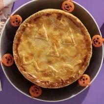 Foto da receita de Torta Folhada Cremosa de Frango com Abóbora para o Dia das Bruxas servida em um prato grande preto com decoração de halloween em volta