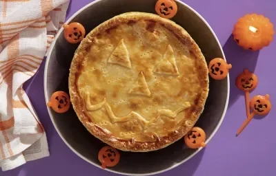 Foto da receita de Torta Folhada Cremosa de Frango com Abóbora para o Dia das Bruxas servida em um prato grande preto com decoração de halloween em volta Foto da receita de Torta Folhada Cremosa de Frango com Abóbora para o Dia das Bruxas servida em um prato grande preto com decoração de halloween em volta