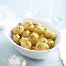 fotografia em tons de branca e azul de uma bancada vista de cima, contém um recipiente redondo e branco com bolinhas de batatas e alecrim por cima