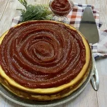 Foto da Receita de Torta de Ricota com Goiabada. Observa-se uma torta inteira com uma espátula prateada ao lado direito em cima de uma tábua de madeira clara.