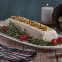 Foto da receita de Mousse de Queijos, num prato branco, sobre uma bancada de madeira toda decorada com motivos natalinos, uma vez branca acesa ao fundo e um tecido colorido de natal como guardanapo