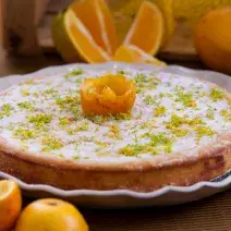 Foto aproximada da receita de bolo de casca de laranja, servido em um prato e decorado com açúcar e raspas de laranja.