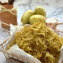 Foto da receita de batata palha caseira. Observa-se a batata palha em uma cestinha de servir rose gold em cima de um mármore branco.