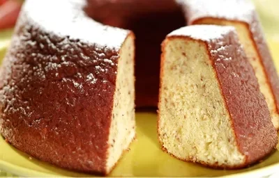 Fotografia em tons de verde em uma mesa de madeira com uma toalha verde quadriculada. Ao centro, um suporte para bolo verde com o bolo de pinhão em cima dele.