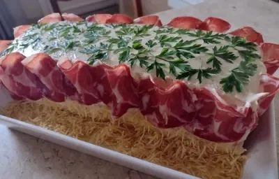 Foto da receita de pão surpresa decorado com folhas verdes por cima e presunto de parma cobrindo os lados, além de batatas palhas ao fundo da travessa Foto da receita de pão surpresa decorado com folhas verdes por cima e presunto de parma cobrindo os lados, além de batatas palhas ao fundo da travessa