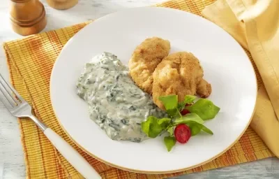 Foto da receita de Creme de Espinafre Sem Lactose. Observa-se um prato branco com o creme do lado esquerdo e, ao lado direito, uma posta de peixe frito com salada.