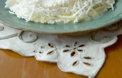 Foto com uma tapioca de Leite Moça e coco em um prato na cor azul, em cima de uma toalha branca decorada Foto com uma tapioca de Leite Moça e coco em um prato na cor azul, em cima de uma toalha branca decorada