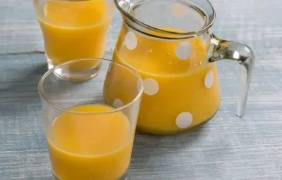 Fotografia em tons de azul e amarelo com uma jarra de vidro com bolinhas brancas e dois copos contendo suco de frutas, tudo sobre bancada em tons de azul. Fotografia em tons de azul e amarelo com uma jarra de vidro com bolinhas brancas e dois copos contendo suco de frutas, tudo sobre bancada em tons de azul.