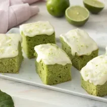 Foto de receita de Bolo de Couve com Calda de Limão. Observa-se uma tábua branca com 6 pedaços de bolo verde com calda de limão.