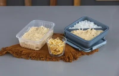 Foto da receita de fricassê de frango, servida em potinhos de marmita, com arroz e batata palha, sobre uma tábua de madeira em uma bancada cinza.