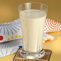 fotografia em tons de bege, branco azul e vermelho tirada de um copo transparente com a bebida dentro ao fundo um pano branco com desenhos em azul, vermelho e amarelo.