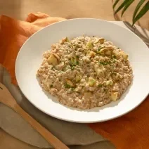 Foto da receita de risoto de abobrinha vegano servida em um prato de cerâmica com um garfo de madeira ao lado sobre um paninho laranja