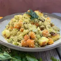Foto da receita de Cuscuz Marroquino. Observa-se um prato de cerâmica claro redondo contendo a receita finalizada com um ramo de salsa verde.