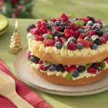Foto da receita de bolo pelado naked cake natalino sem glúten servida sobre uma base bege em cima de uma mesa verde com decorações de natal, além de um pano vermelho com uma espátula de madeira em cima
