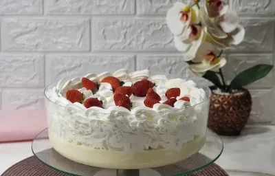Fotografia em tons de rosa em uma bancada de mármore com um pano rosa ao fundo e ao centro uma tampa de bolo com o bolo afogado dentro e decorado com chantilly e morangos. Fotografia em tons de rosa em uma bancada de mármore com um pano rosa ao fundo e ao centro uma tampa de bolo com o bolo afogado dentro e decorado com chantilly e morangos.