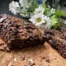 Imagem da receita de Brownie Rápido de Chocolate com Aveia sobre uma mesa e atrás umas flores