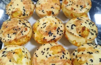 Foto da receita de Pão de Queijo Funcional. Observa-se um prato branco quadrado com 9 unidades de pão de queijo polvilhados de gergelim preto em cima.