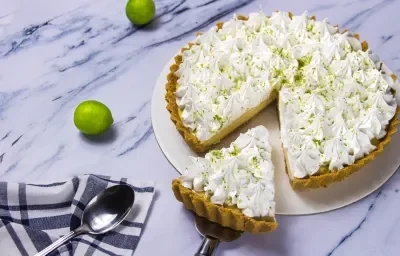 Fotografia de uma torta de limão  com um pedaço retirado em evidência sobre uma mesa de mármore.