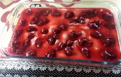 Foto em tons de vermelho da receita de mousse de frutas servida em um refratário de vidro grande com calda de frutas vermelhas por cima