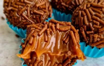 Foto da receita de Brigadeiro Maravilhoso. Observa-se quatro brigadeiros com granulado em forminhas azuis. O da frente está mordido para mostrar a cremosidade.