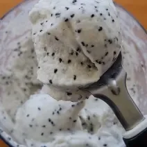 Foto da receita de Sorvete de Pitaya. Obesrva-se uma colher de sorvete com o sorvete de pitaya dentro, branco com sementes, e um pote atrás da colher