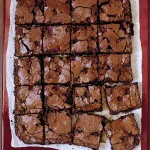 fotografia em tons de marrom e branco de uma bancada vista de cima, contém um pano branco e por cima pedaços quadrados de bolo de chocolate