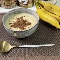 Imagem da receita de Mingau Proteico em um bowl, sobre uma mesa e ao lado uma banana e colher