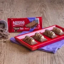 Fotografia mostra quatro barrinhas de chocolate com biscoitos, cobertas com um creme branco e decorada com chocolate derretido.