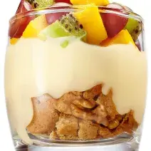 fotografia tirada de um copo transparente com biscoitos triturados, leite MOÇA e frutas por cima.