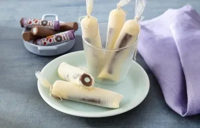 Foto da receita de geladinho algodão doce servida em 5 porções dentro de um pote transparente em cima de um prato de porcelana com um paninho lilás e algumas unidades de baton ao fundo Foto da receita de geladinho algodão doce servida em 5 porções dentro de um pote transparente em cima de um prato de porcelana com um paninho lilás e algumas unidades de baton ao fundo