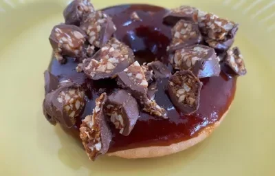 Fotografia de um donuts coberto com caramelo e um pedaço de um bombom de chocolate com caramelo por cima.