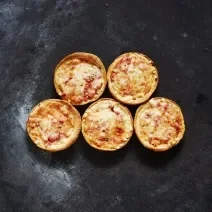Fotografia vista de cima de cinco mini pizzas de mozarela sobre uma bancada preta com um pouco de farinha.