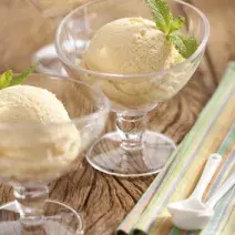 Em uma mesa de madeira contém duas taças de vidro com uma bola de sorvete cada.