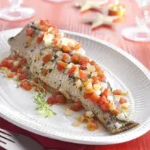 Fotografia em tons de vermelho e branco de uma bancada vermelha, sobre ela um prato branco com o peixe  e um garfo. Ao fundo taças de água.