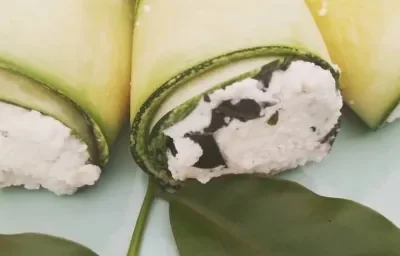 Foto da Receita de Canelone de Abobrinha com Ora-pro-nóbis. Observa-se três canelones recheados de perto, decorados com uma folha de ora-pro-nobis.