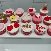 Fotografia em tons de rosa com vários cupcakes ao centro. Cada cupcake possui uma decoração específica, alguns feitos de coração, outros de flores e outros de lacinhos.