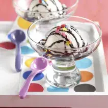 fotografia em tons de rosa e branco tirada de uma bandeja branca com duas taças e ambas contém um bola de sorvete com calda de chocolate.