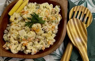 Foto da Receita de Macarronese. Observa-se um recipiente de madeira escuro com a macarronese. Ao lado direito, duas colheres grandes de servir. Foto da Receita de Macarronese. Observa-se um recipiente de madeira escuro com a macarronese. Ao lado direito, duas colheres grandes de servir.