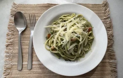 Imagem da receita de Macarrão com Espinafre e Tomate Cereja, em um prato branco e ao lado os talheres Imagem da receita de Macarrão com Espinafre e Tomate Cereja, em um prato branco e ao lado os talheres