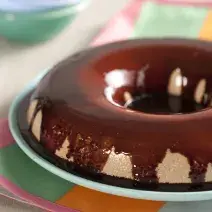 foto em tons de branco e marrom tirada de frente, contém um prato redondo azul com uma sobremesa gelada de chocolate com calda de chocolate por cima