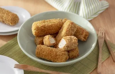Foto da receita de Bolinho de Tofu. Observa-se uma tigela de porcelana verde clara com os bolinhos empanados dentro, sendo que um está cortado no meio. A tigela está sobre uma rede de sushi e uma superfície de madeira. Foto da receita de Bolinho de Tofu. Observa-se uma tigela de porcelana verde clara com os bolinhos empanados dentro, sendo que um está cortado no meio. A tigela está sobre uma rede de sushi e uma superfície de madeira.