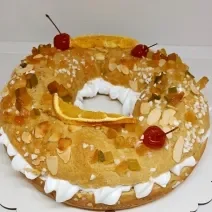 Foto da receita de Rosca de Reis. Observa-se uma rosca recheada com chantilly e decorada com frutas secas, cereja e amêndoas laminadas.