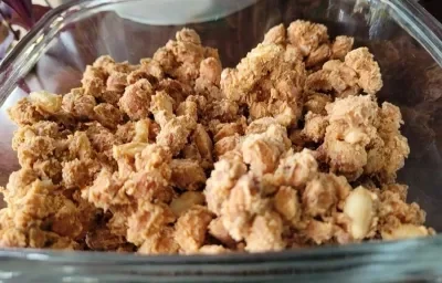 Foto em tons de bege da receita de amendoim perfumado servida em uma travessa de vidro retangular sobre uma mesa de madeira Foto em tons de bege da receita de amendoim perfumado servida em uma travessa de vidro retangular sobre uma mesa de madeira