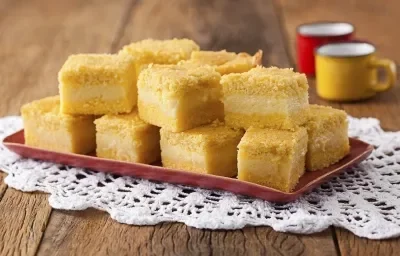 8 pedaços quadrados de bolo amarelo com uma lista branca no meio, dispostos em um prato vermelho que está em cima de uma toalha branca 8 pedaços quadrados de bolo amarelo com uma lista branca no meio, dispostos em um prato vermelho que está em cima de uma toalha branca