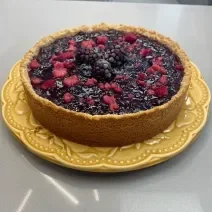 Foto da receita de torta ridícula servida em uma porção grande decorada com frutas vermelhas em cima. Torta está sobre um prato amarelo em cima de uma bancada cinza