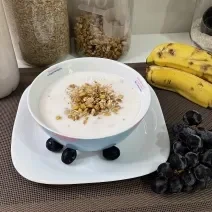 Imagem da receita de Iogurte Caseiro de Morango em um bowl, sobre uma mesa com bananas e uvas ao lado