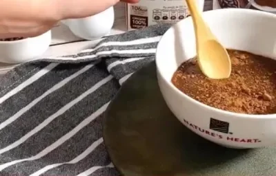 Foto da receita de Brigadeiro Plant-based. Observa-se uma tigela branca com o brigadeiro de colher dentro e as embalagens de Natures Heart atrás.